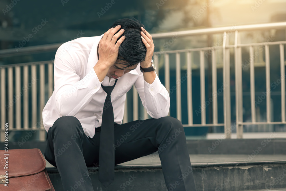 Asian young businessman stress sitting in front office with his hands covering his head against. Asian young businessman stress sitting in front office with his hands covering his head against.