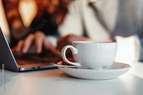 Man and woman working in front of the laptop. Tea cup is on foreground.