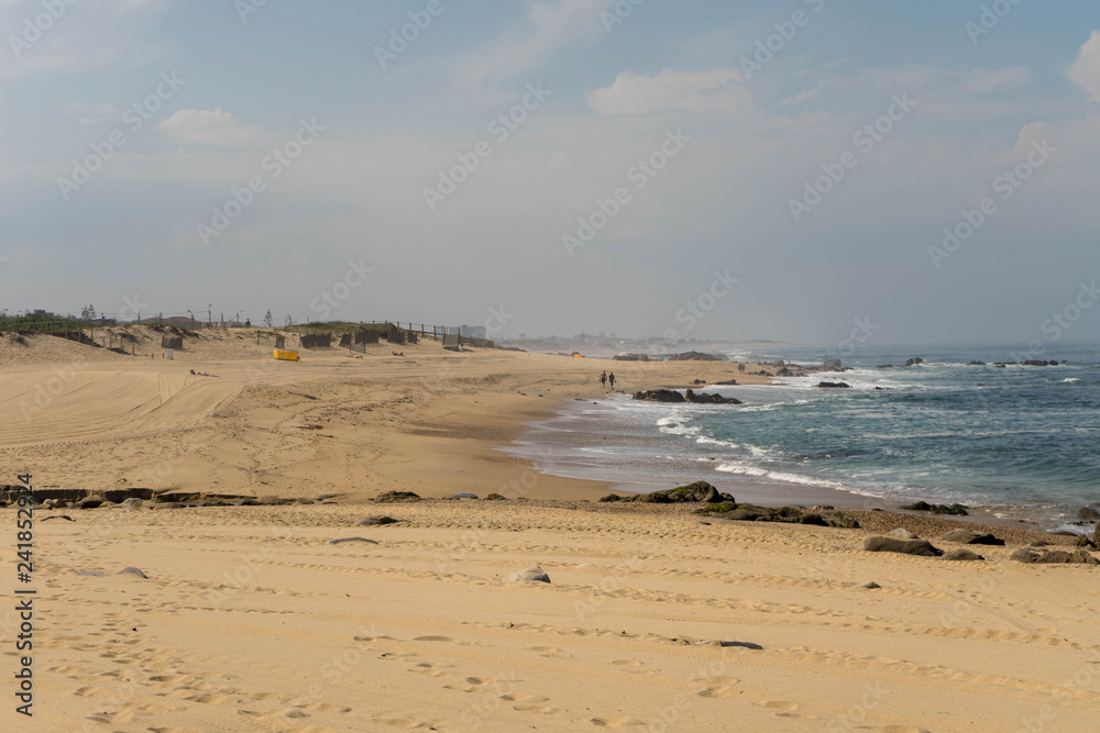 Ocean beach in Madalena, near Porto, Portugal. Yellow sand and lots of big rocks, big waves on atlantic ocean.