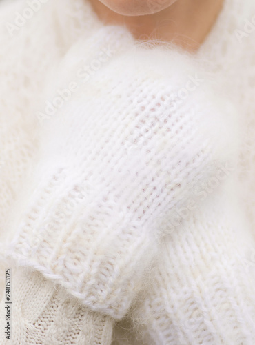Closeup view of female hands wearing white fluffy cozy knitted mittens while standing outdoors on cold frosty winter day. Vertical color photography.