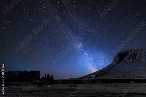 Vibrant Milky Way composite image over landscape of Norber Ridge and stone barn in Yorkshire Dales National Park