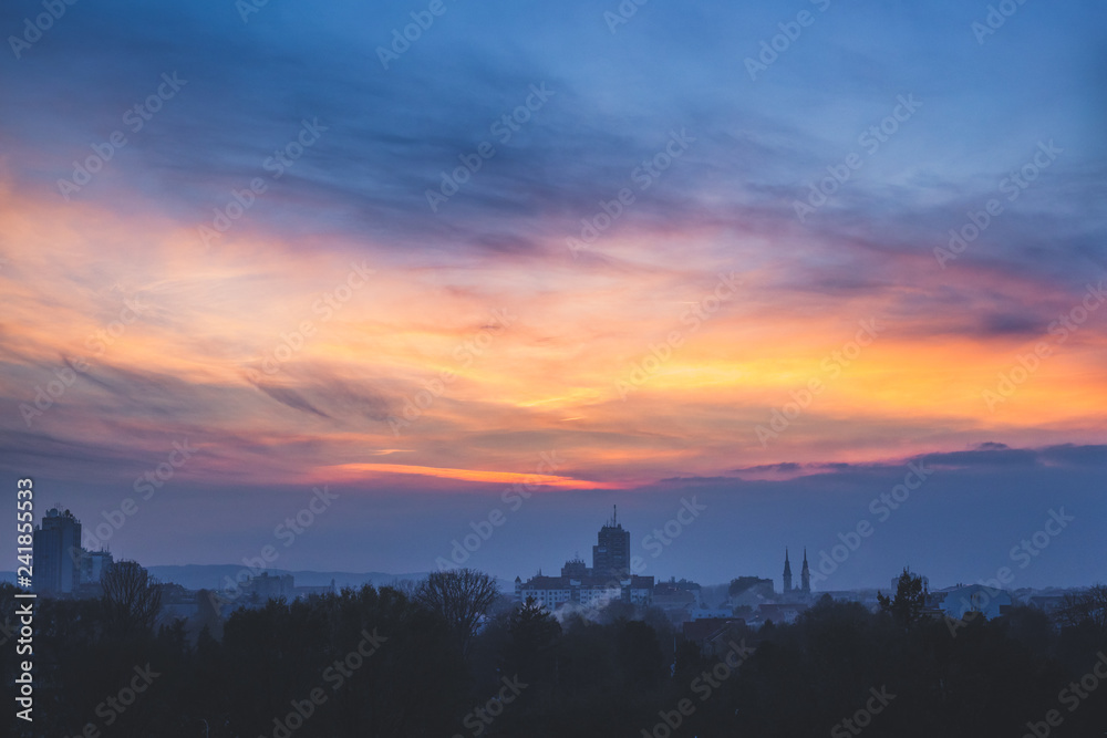 Dim winter twilight. Clouds at sunset over dark industrial town.