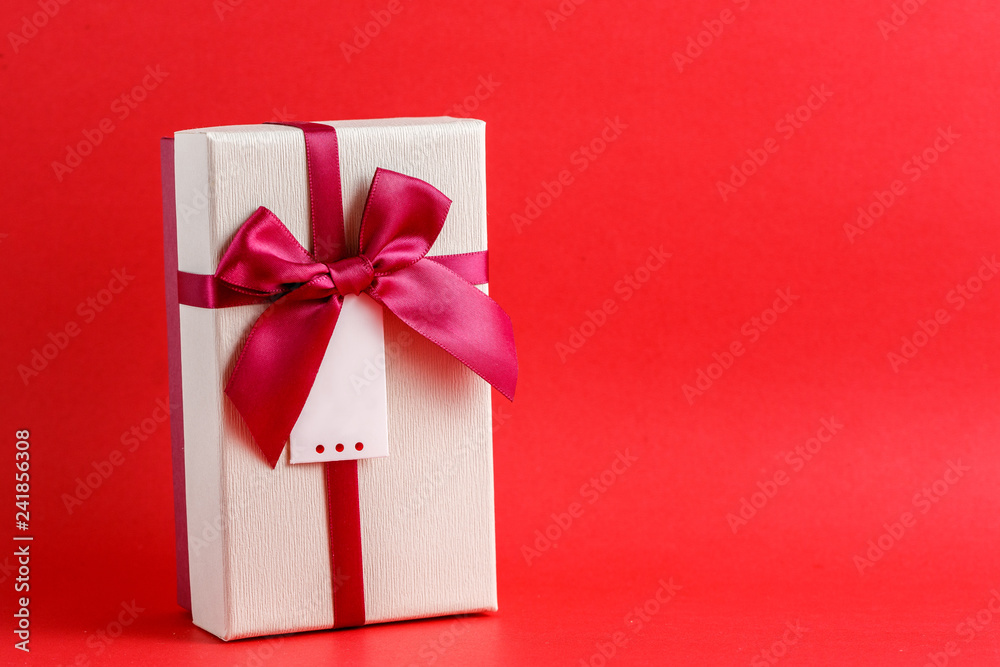 Gift box with a ribbon on a red background. The concept is suitable for love stories, birthdays and Valentine's Day Gift box with a ribbon on a red background. The concept is suitable for love stories, birthdays and Valentine's Day