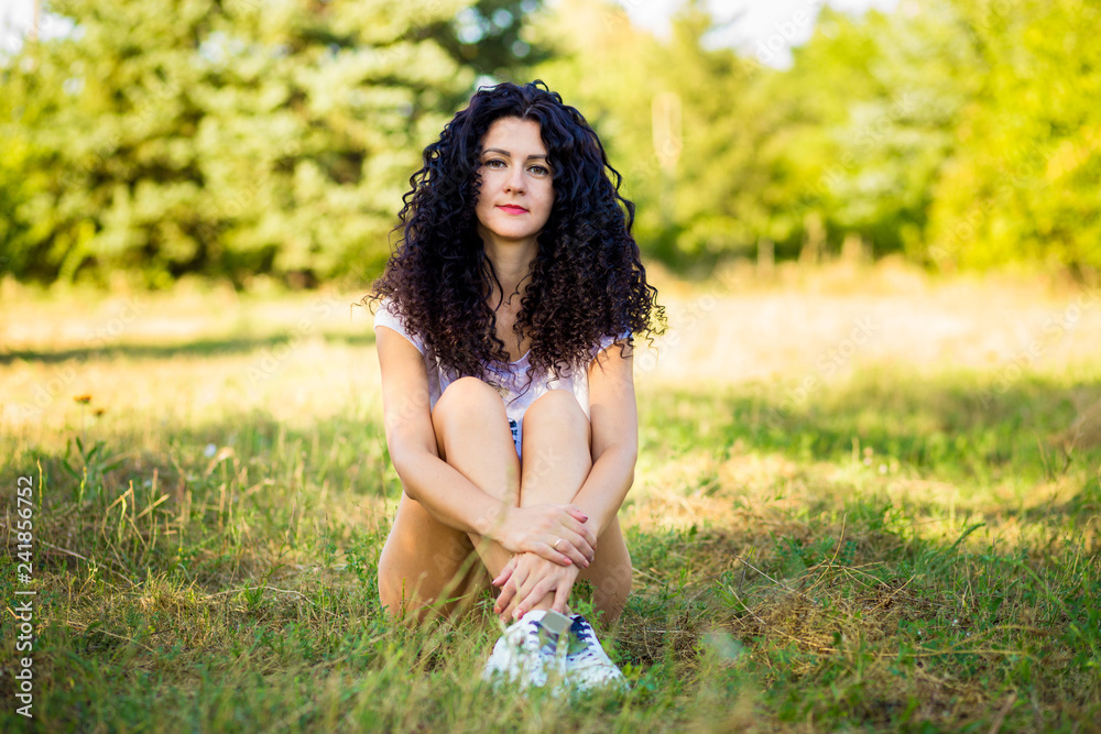Pretty curly woman posing on grass in sunny day Pretty curly woman posing on grass in sunny day