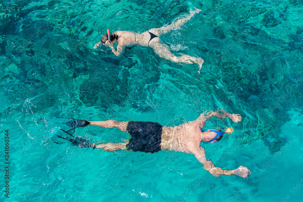 Man and women snorkeling in tropical water on vacation. Woman swimming in blue sea. Snorkeling girl in full-face snorkeling mask. People in flippers and masks in the clear sea.
