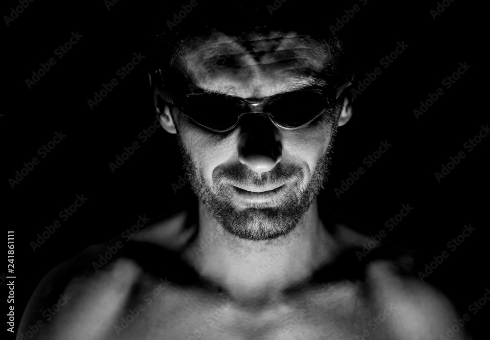 Portrait of unshaven adult caucasian man in swimming glasses. He smiles and looks straight to watcher. Black and white shot, low-key lighting. Isolated on black. Portrait of unshaven adult caucasian man in swimming glasses. He smiles and looks straight to watcher. Black and white shot, low-key lighting. Isolated on black.