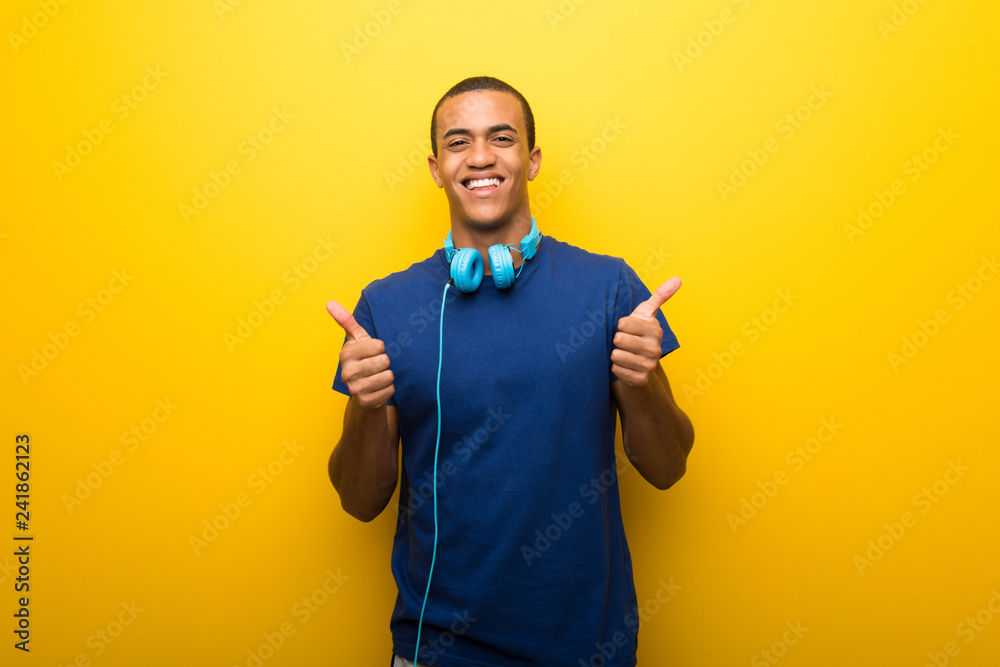 African american man with blue t-shirt on yellow background giving a thumbs up gesture with both hands and smiling African american man with blue t-shirt on yellow background giving a thumbs up gesture with both hands and smiling