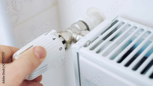 A man regulates the temperature in the house with a thermostat on the radiator. 4K video with shallow depth of field focus.