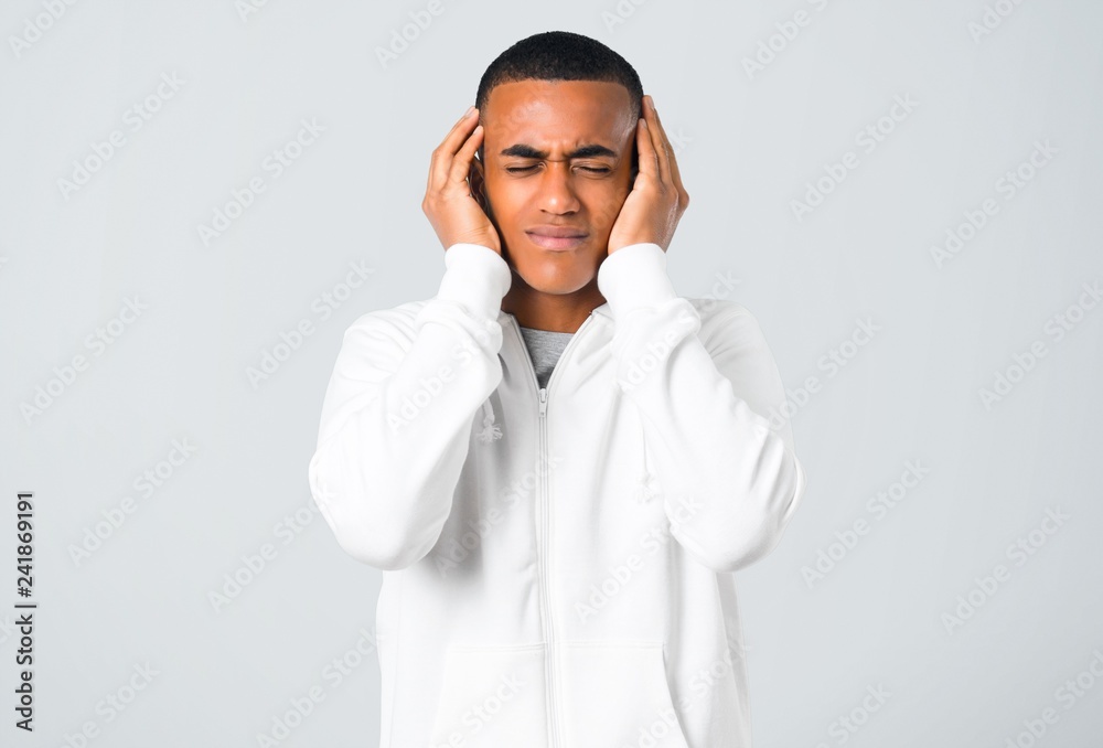 Dark-skinned young man with white sweatshirt covering both ears with hands on grey background Dark-skinned young man with white sweatshirt covering both ears with hands on grey background