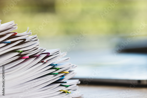Close up pile of unfinished homework assignment stacked in archive with colorful paper clips on table in school waiting to be managed and inspected. Stack of paperwork. Education and business concept.