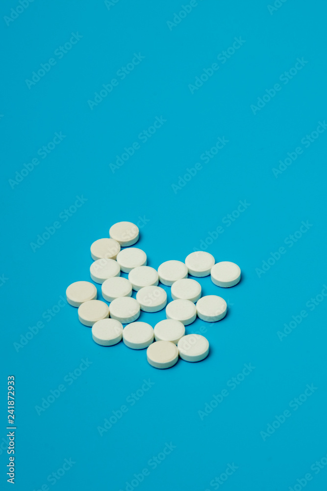 a bunch of pills on an blue background. A bunch of white pills on a turquoise background. copy space. vertical photo