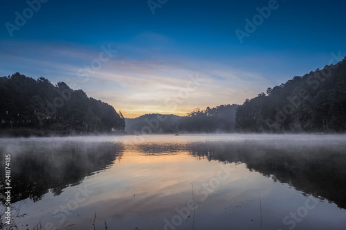 sunrise at Pang Oung, beautiful lake view misty morning of soft mist moving on the water with reflection of pine forest on water and colorful of sun light in the sky background, Mae Hong Son, Thailand