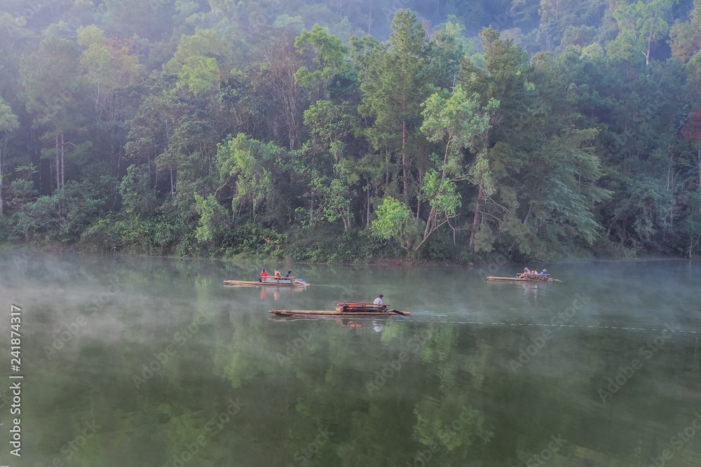 sunrise at Pang Oung reservoir, lake view morning of tourists in bamboo-rafting around with the mist and pine forest background, Pang Oung Lake, Mae Hong Son, northern Thailand.