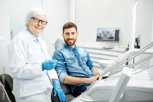Portrait of a handsome male patient in blue shirt with elderly woman dentist in the dental office