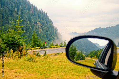 rear view mirror with a soft focus reflection of a mountain road against backdrop of the blue cloudy sky