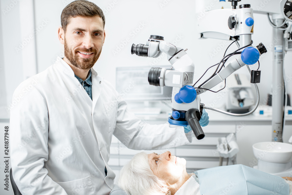 Portrait of a male dentist during the examination with professional microscope at the surgery dental office Portrait of a male dentist during the examination with professional microscope at the surgery dental office