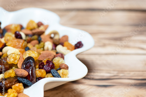 Mix of nuts and berries. Dried fruits in white plate on wooden table, copy space for text. Healthy food and vitamins photo