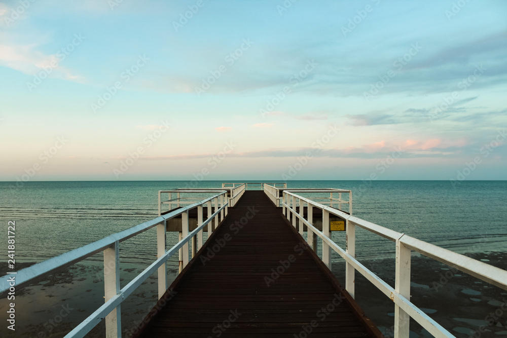 Wooden pier during sunset overseeing the ocean with orange clouds and turquoise sky (Hervey Bay near Fraser Island, Queensland, Australia)