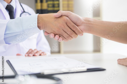 doctor at the clinic giving an handshake to his patient for encouragement and empathy, healthcare and assistance concept.