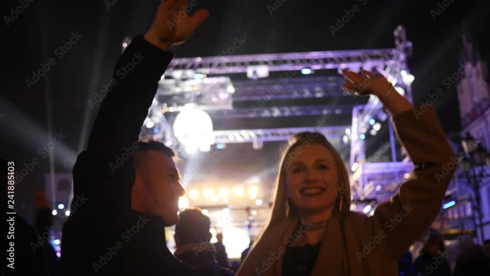 Young couple on music concert raise wave hands dance in rhythm in flashing lights lumiere rays