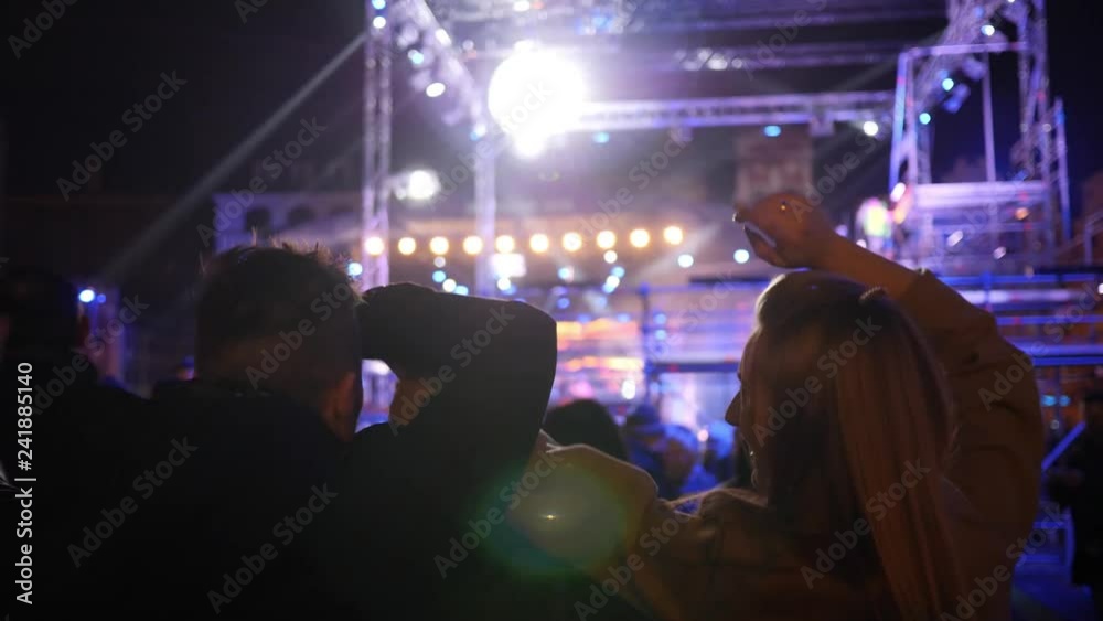 Young couple on music concert raise wave hands in rhythm in flashing lights lumiere rays Young couple on music concert raise wave hands in rhythm in flashing lights lumiere rays
