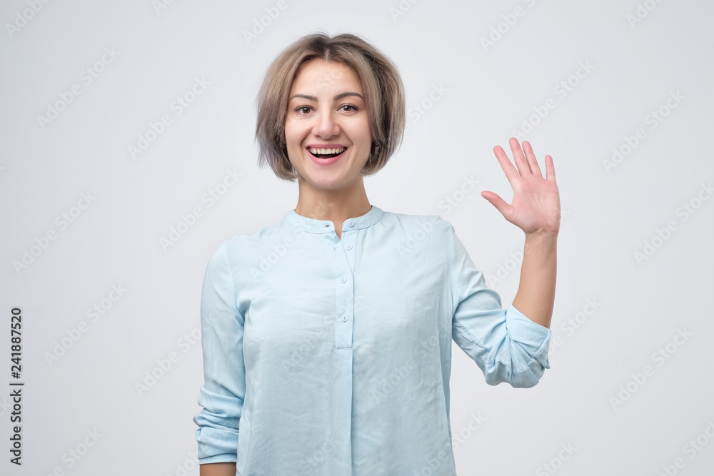 Friendly european female entrepreneur, smiling broadly while waving raised palm Friendly european female entrepreneur, smiling broadly while waving raised palm