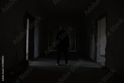 A woman from backside standing in dark corridor of abandoned decay building  urbex 