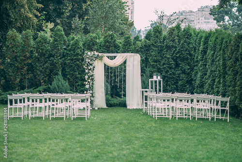 Beautiful wedding set up. Area of the wedding ceremony. Round arch, white chairs decorated with flowers, greenery. Cute, trendy rustic decor. Part of the festive decor, floral arrangement.