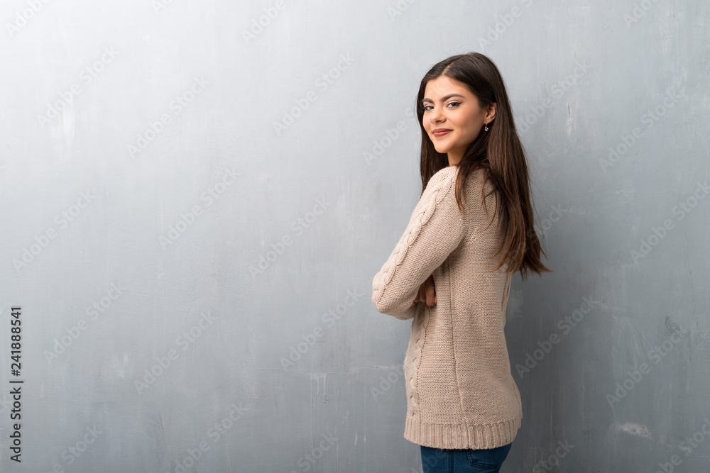 Fototapeta premium Teenager girl with sweater on a vintage wall keeping the arms crossed in lateral position while smiling