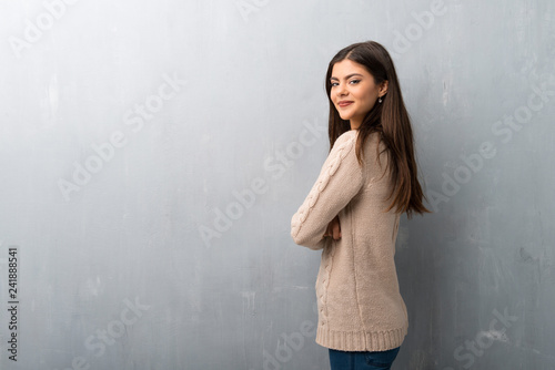 Teenager girl with sweater on a vintage wall keeping the arms crossed in lateral position while smiling