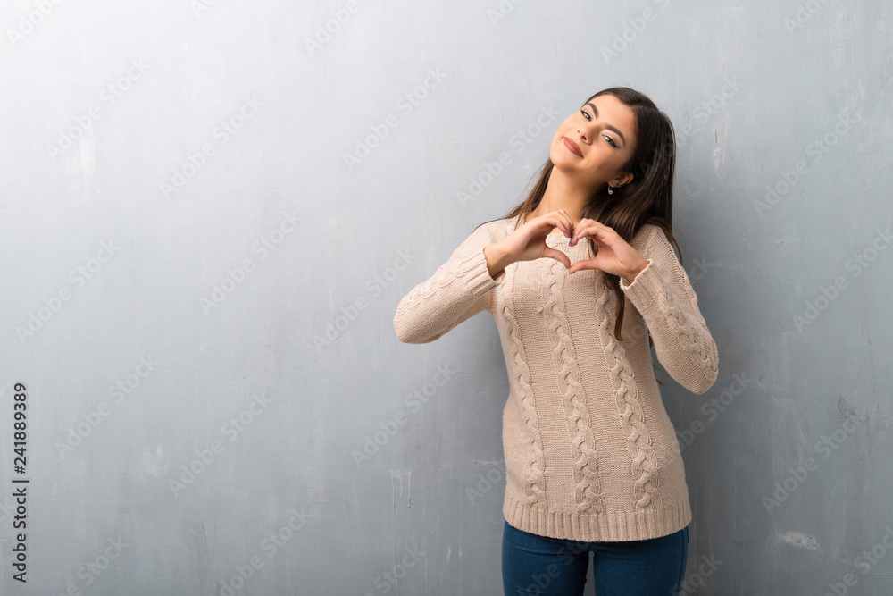Fototapeta premium Teenager girl with sweater on a vintage wall making heart symbol by hands
