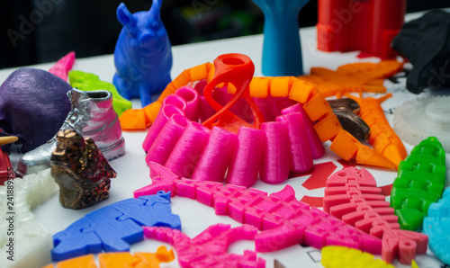 Many bright multi-colored objects printed on 3d printer lie on flat surface close-up. Fused deposition modeling, FDM. Concept modern progressive additive technology for 3d printing.