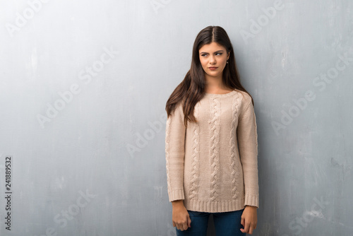 Teenager girl with sweater on a vintage wall feeling upset