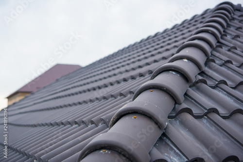 Building a house with a tiled roof. Directing wooden roof beams. Gray roof tiles and chimney of red brick. Unfinished house. Attic under the roof of the house. Round roof slope.