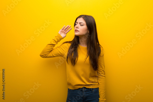 Teenager girl on vibrant yellow background listening to something by putting hand on the ear