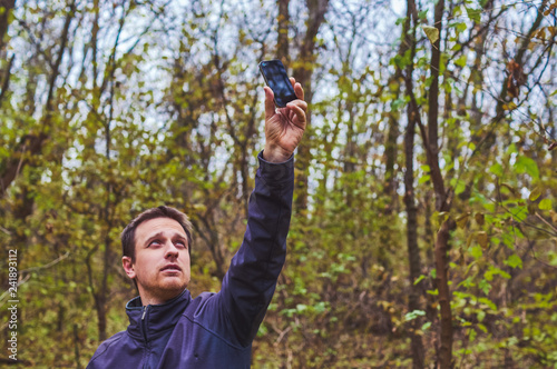 Man with his mobile smart phone searching for reception signal in the forest.