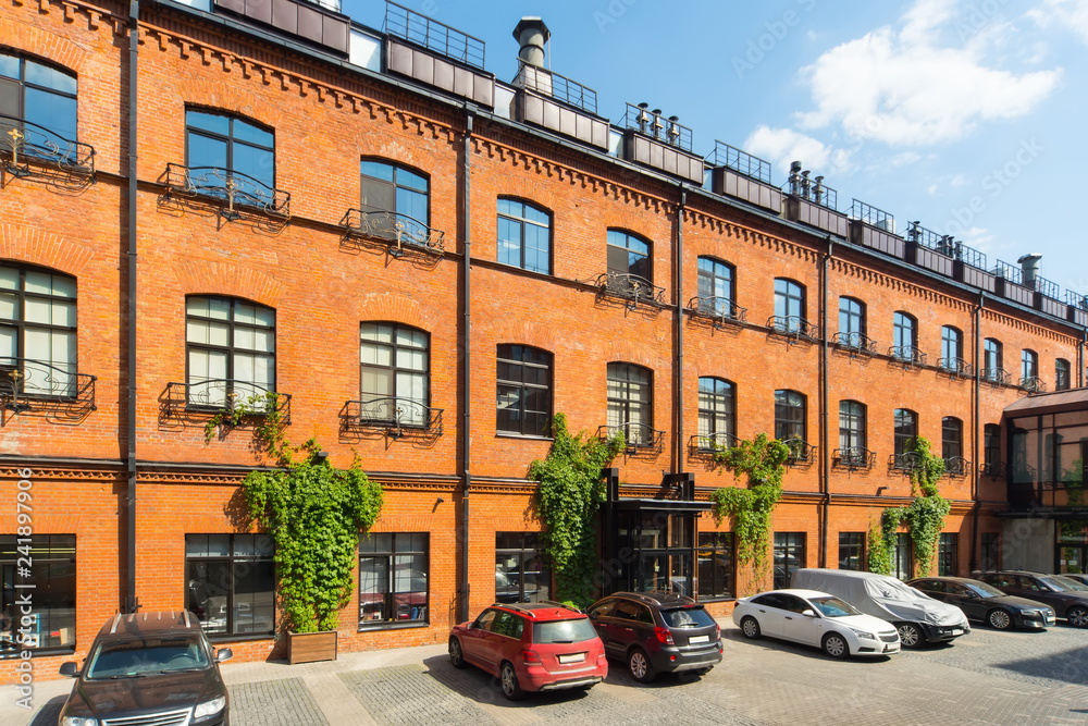 Huge red brick classic industrial building facade with multiple windows. Industrial background. Loft inspiration. Parked cars