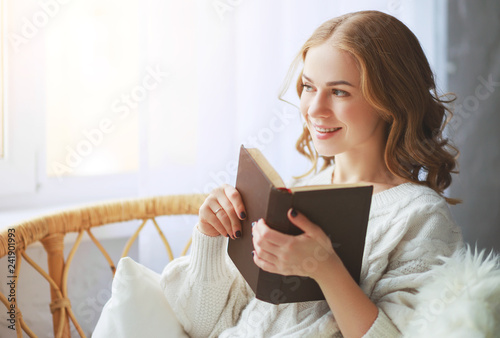 happy young woman reading a book by window