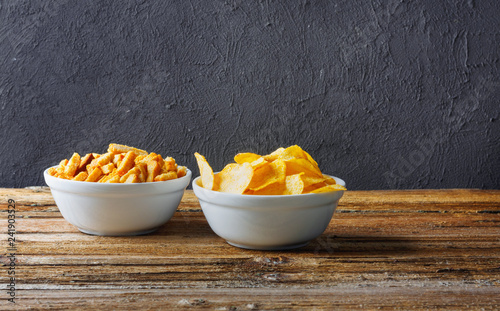 Chips, crackers in bowls on wooden table on brick wall
