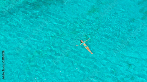 DRONE: Flying above carefree woman floating on her back in middle of the ocean.