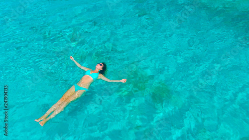 AERIAL  Woman lying on her back on the tranquil surface of the turquoise ocean.