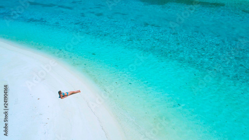DRONE: Flying above female tourist in bikini lying on the beach and sunbathing.