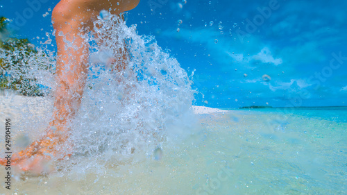 CLOSE UP: Unrecognizable woman splashes water as she runs along tropical beach. © helivideo