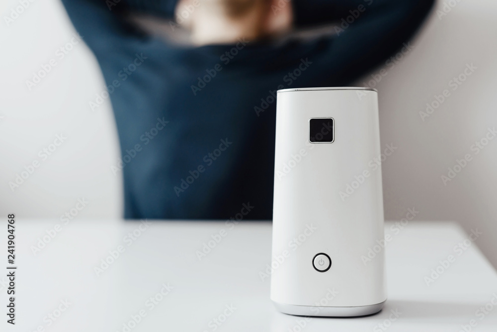 White ionizer is standing on a white table in the background of a relaxed man. Concept of caring for fresh air in the apartment, in the office. Caring for well-being and health. Air filter. White ionizer is standing on a white table in the background of a relaxed man. Concept of caring for fresh air in the apartment, in the office. Caring for well-being and health. Air filter.