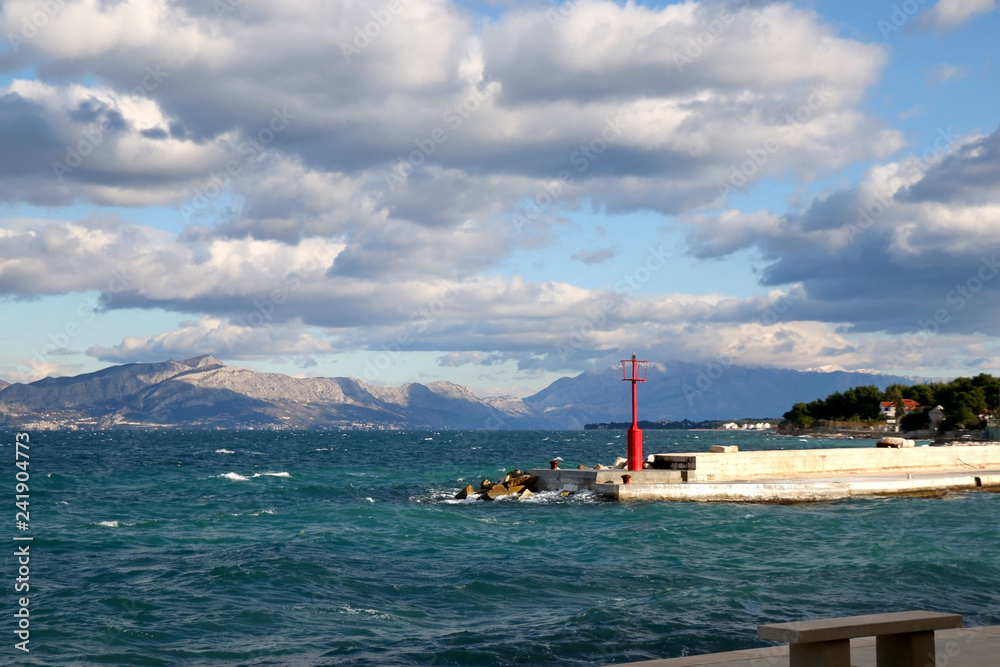 Small red lighthouse on the pier in Sutivan, island Brac, Croatia. Windy and cloudy weather, beautiful landscape.