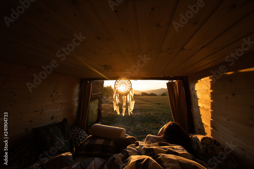 Beautiful view from camper van during sunrise in summer with woman in a bed