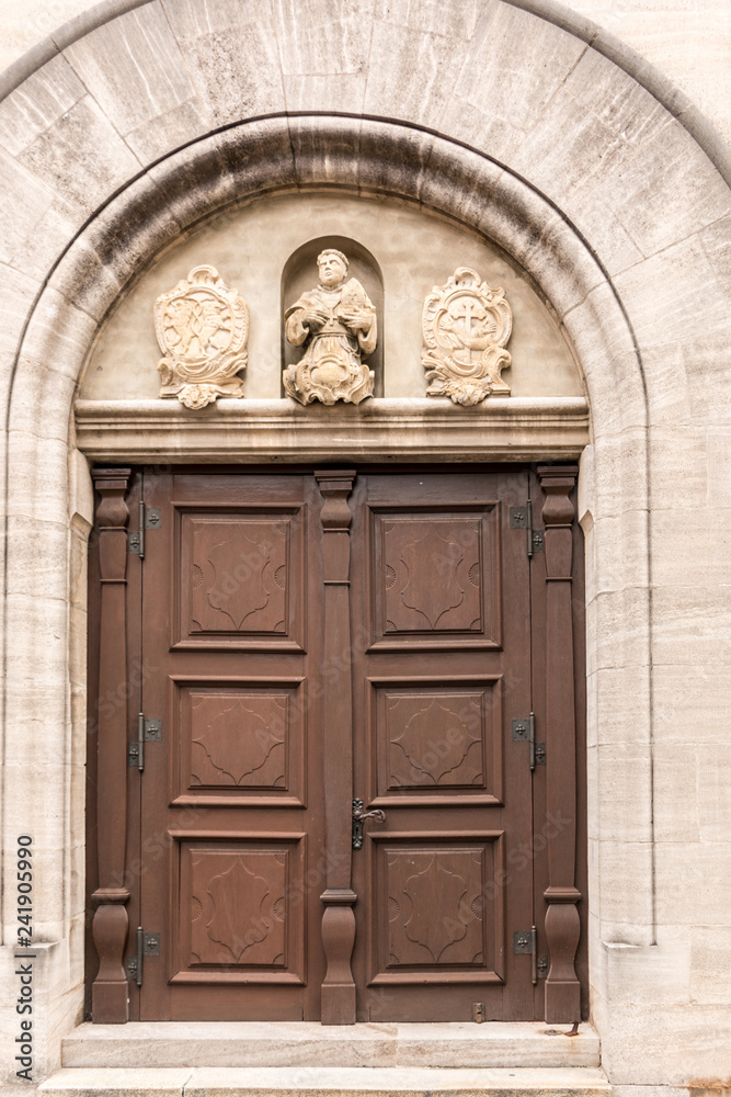 Old door of a historical building with statues and coats of arms made of stone