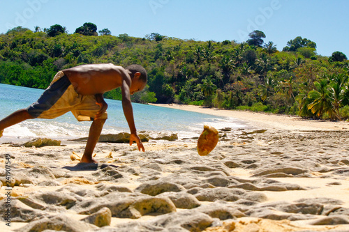 Poor malagasy boy breaking coconuts on the beach