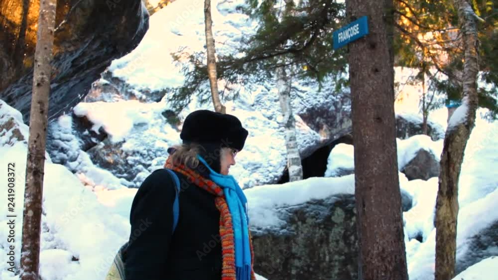 Old woman in the forest in winter looking happy, pointing at something in the middle of the forest, in wintertime - traveling up