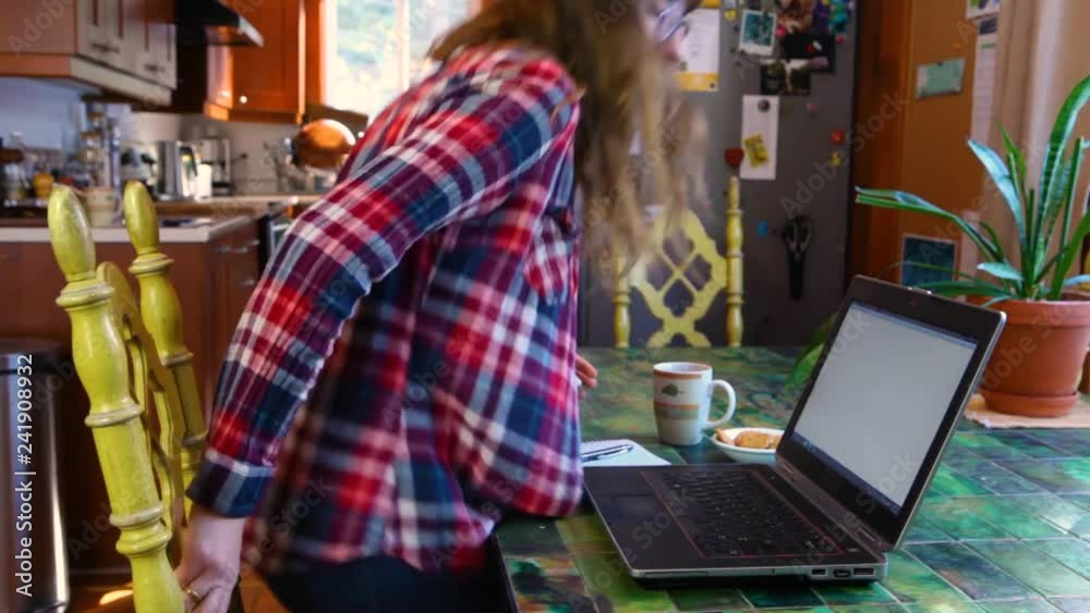 Woman at the table working with laptop. Girl with glasses wearing a checkered shirt, sits in front of her laptop with cookies and coffee, and starts typing text. Fixed wide angle scene Woman at the table working with laptop. Girl with glasses wearing a checkered shirt, sits in front of her laptop with cookies and coffee, and starts typing text. Fixed wide angle scene